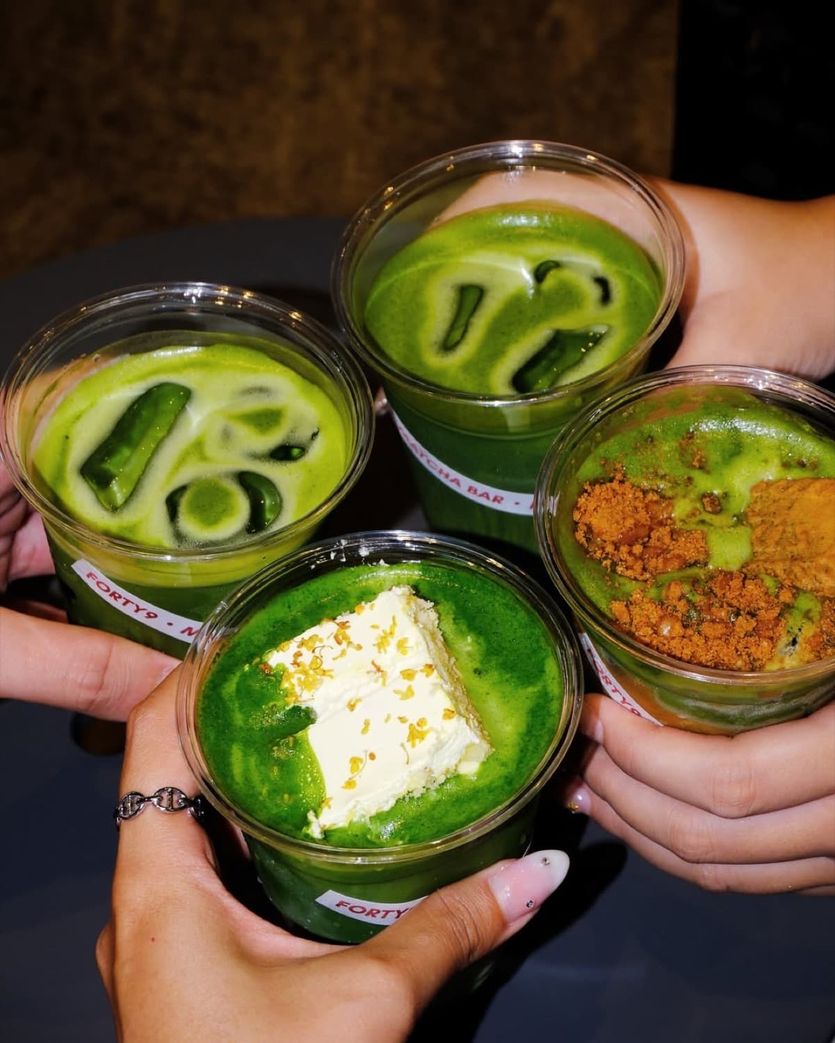 Four hands holding vivid green matcha drinks at Forty9 Matcha Bar, City Gate