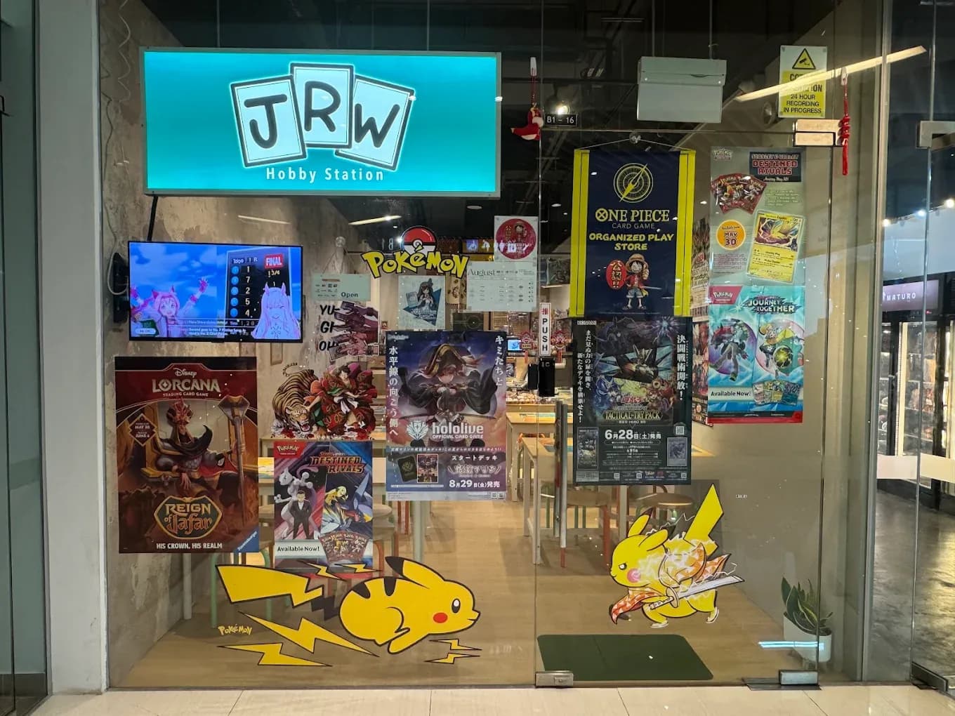 The JRW Hobby Station storefront at City Gate, lit sign over Pokemon and One Piece trading-card displays